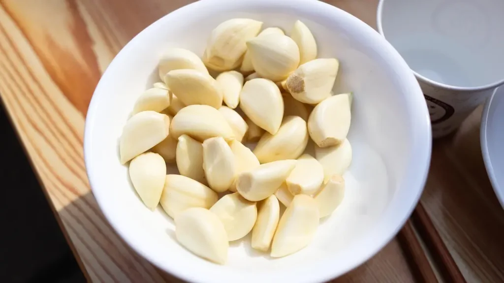Gousses d'ail pelées dans un bol blanc sur table en bois, prêtes à cuisiner, montrant l'intérieur blanc