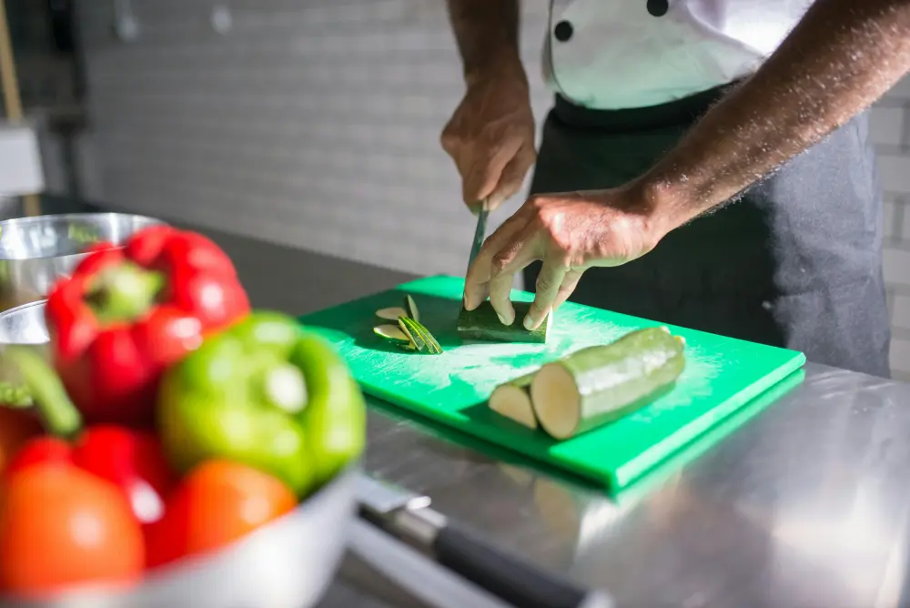 Chef coupe courgette fraîche sur planche verte, préparation cuisine légumes bio