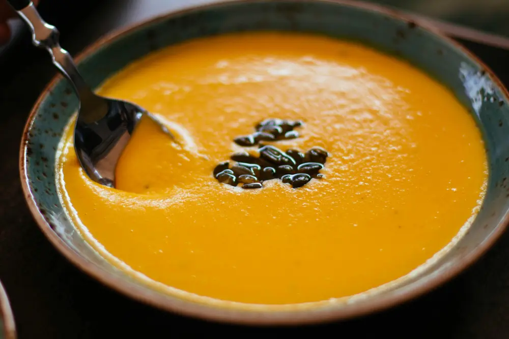 Cultiver les courges : le guide complet du semis à la récolte 7 Velouté de potiron orange crémeux avec garniture de graines de courge dans un bol en céramique turquoise