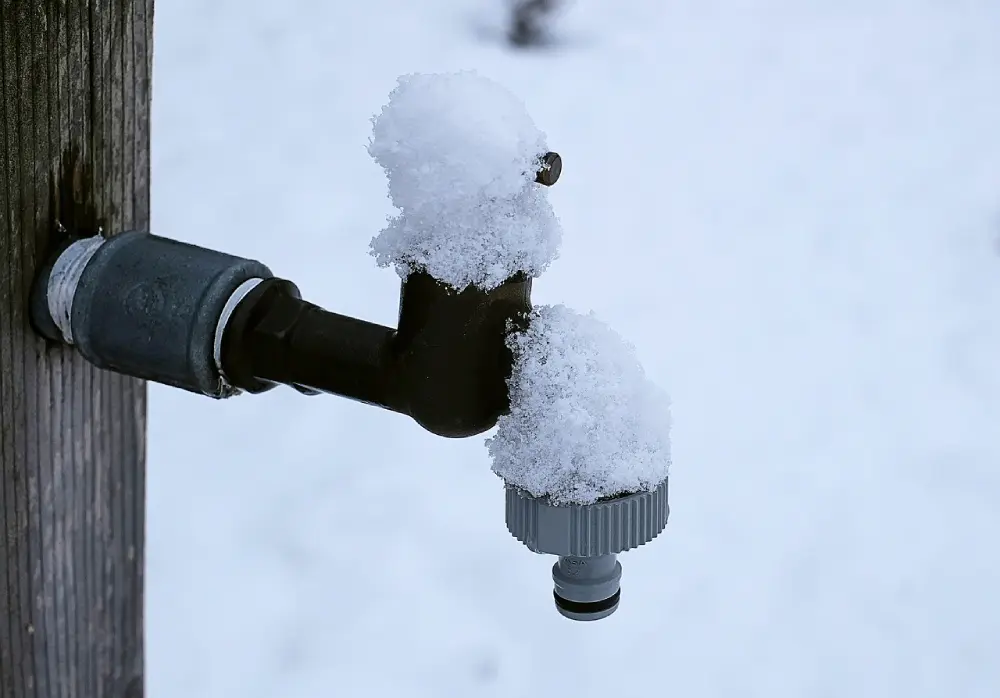 Robinet extérieur et tuyau d'arrosage recouverts de neige à protéger en décembre