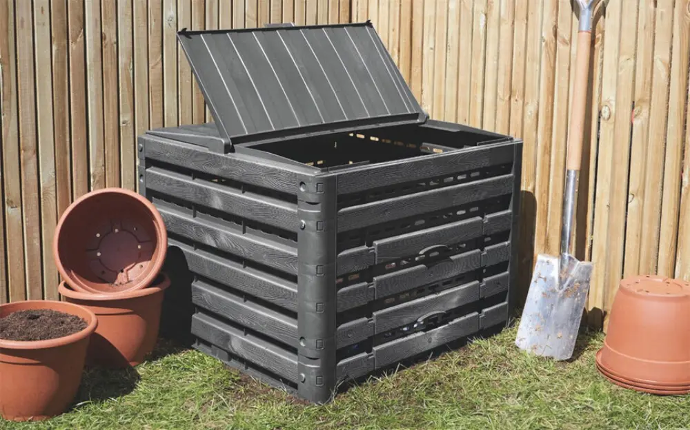 Composteur bac plastique noir avec couvercle ouvert installé dans jardin potager