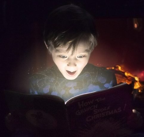 Enfant lisant un livre dans l'obscurité, son visage illuminé par une lueur magique